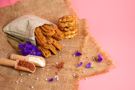 Brown cookie stick shape in burlap bag and other with flour cocoa dried flower on pink background with copy spaceの写真素材