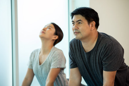 Two Asian couple husband wife practice Yoga pose Cobra or Bhujangasana in gym near window close upの写真素材