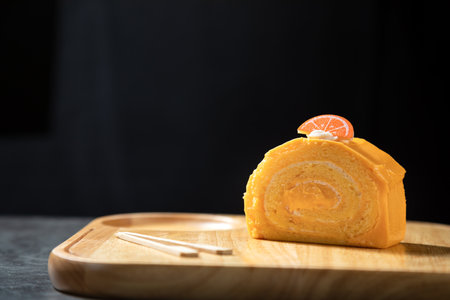 Orange roll cake topping with fresh whipped cream and snack paste on wooden board.の写真素材