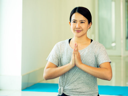 One Asian young female adult sitting holding hands for practice Yoga pose with Prayer Hands close up with copy space in gym near windowの写真素材