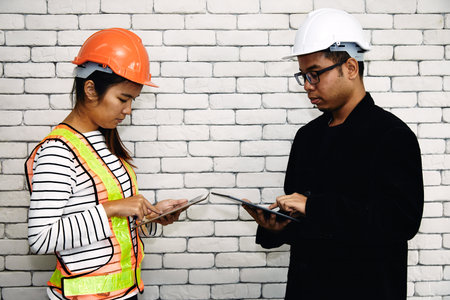 Two engineer and contractor in hard hats using tablets to discuss work details in front of a white...