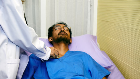 Doctor examines patient lying in hospital bed, checking vital signs with stethoscope during medical assessmentの写真素材