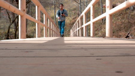Low-angle shot of one man walking with camera walking on bridge, focus on the planksの写真素材