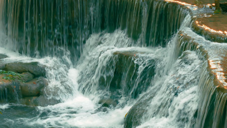 Detailed view of a cascading waterfall flowing over tiered rock formations, creating a serene and...