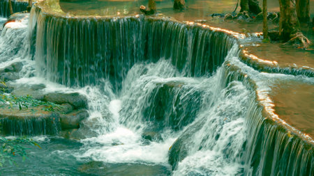 Beautiful cascading waterfall flowing over tiered rock formations, surrounded by lush greenery in a tranquil forestの写真素材