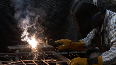 A welder in safety gear fuses metal pieces, producing glowing sparks and thick smoke during an...