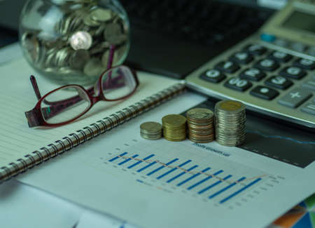 Growth up chart paper showing the results of successful financial planing investment. Glass coins notebook calculator and laptop - business, banking, finance and investment conceptの写真素材