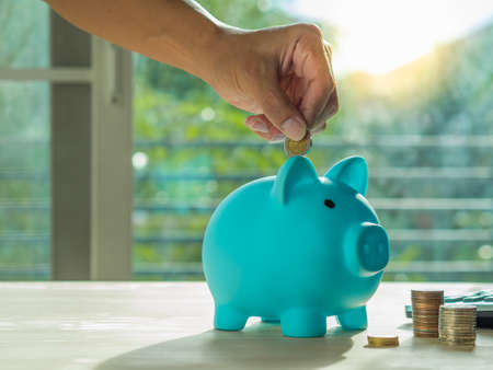 Hands puts a coin in a blue  piggy bank. The concept of saving money or savings, investmentの写真素材
