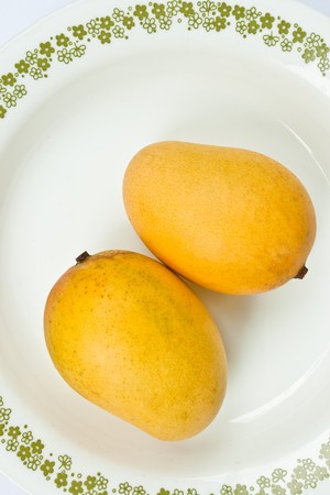 Ripe golden mangoes on white dishの写真素材