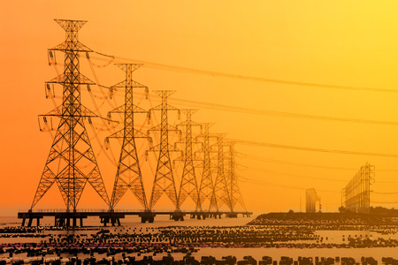 High voltage electric transmission tower energy pylon in the sea at sunset.