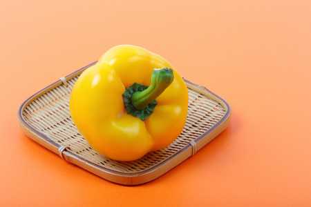 Beautiful of sweet yellow bell pepper isolated in bamboo basket on orange background.の写真素材