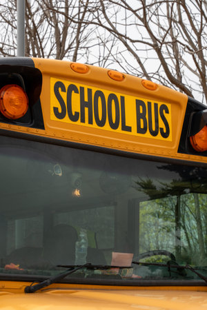 Horizontal close-up view of a yellow school bus in the USA showing the â€˜School Busâ€™ sign on the front windshield, highlighting student transportation and road safety