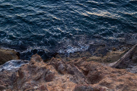 The dark blue sea collides with the rock. Top view.の写真素材