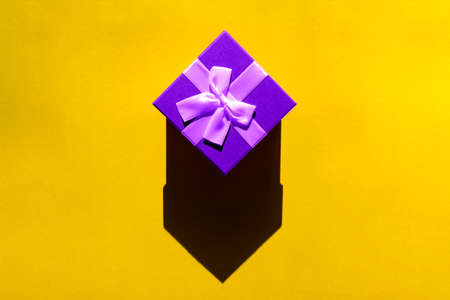 A purple gift with a bow on a bright yellow background. Flatlay.の写真素材