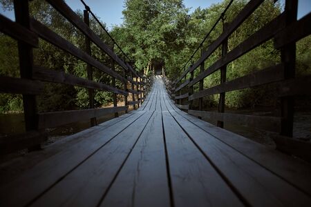 Old wooden bridge leading into green trees over the riverの写真素材