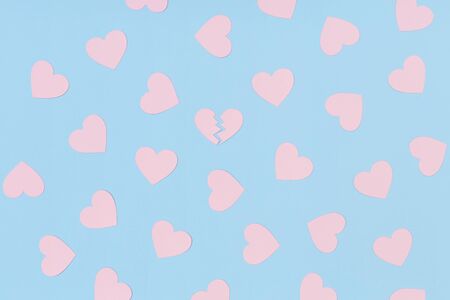 Pattern of pink paper hearts and one broken heart among them on the blue backgroundの写真素材