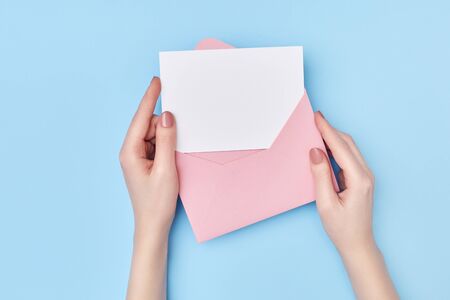 Pink envelope with blank white postcard in womans hands on the blue background. Mail conceptの写真素材