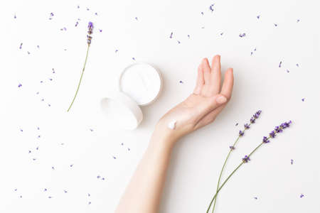 Beautiful well-conditioned female hand moisturizing cream surrounded with lavender flowers on the white background. Hand and body care conceptの写真素材