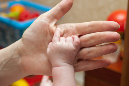 Hand caucasian baby shows a sign of "unity" amid the mother's handsの写真素材