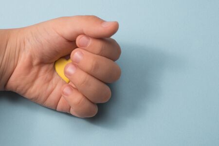 child's hand on a blue background with a yellow heart in the palmの写真素材