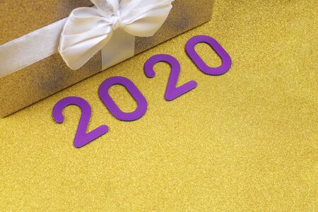 Happy new year 2020. Purple numbers next to the gift with a on a gold background with sequins.の写真素材