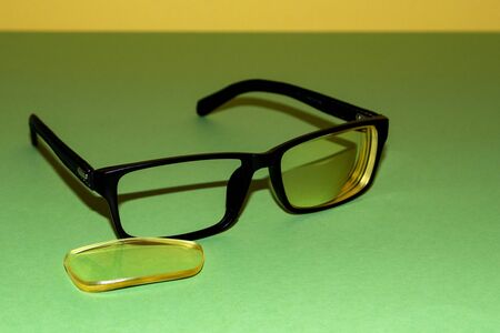Broken glasses lie on a green surface. Nearby lies a yellow lens that has fallen out of the frame. Yellow background backの写真素材