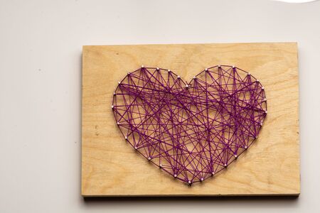 The heart is made of purple threads wrapped on nails embedded in wooden boardの写真素材