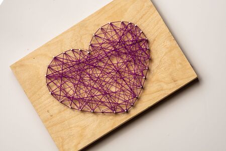The heart is made of purple threads wrapped on nails embedded in wooden board. Diagonally. On a light backgroundの写真素材