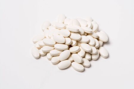 A pile of white oval-shaped tablets on whiteの写真素材
