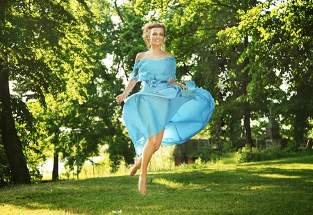 Young charming laughing woman in beautiful dress jumps on meadowの写真素材