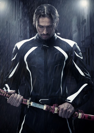 Muscular man holding samurai sword in on a rainy nightの写真素材