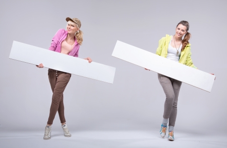 Two happy cheerful girlfriends with white boardsの写真素材
