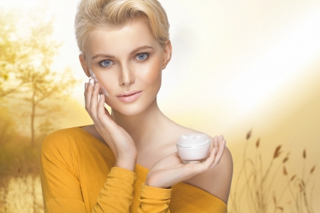 Portrait of young lady applying moisturizer cream on her pretty faceの写真素材
