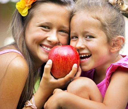 Two sisters sharing a big sweet appleの写真素材