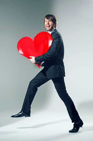 Cheerful young guy holding big heartの写真素材