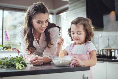 Mother watching her little daughter whisking doughの写真素材