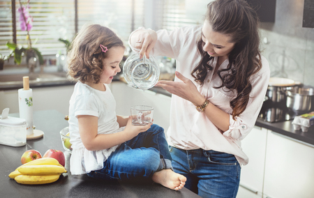 Woman filling a glass with water for her little daughterの写真素材