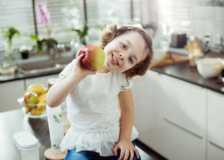 Cheerful kid holding a fresh apple, kitchen shotの写真素材