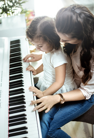 Young mother playing piano with her little daughterの写真素材
