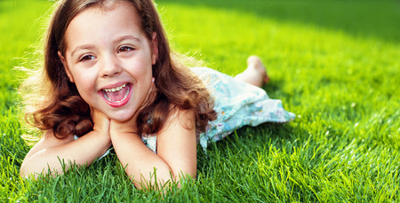 Cute little girl resting on a warm, fresh green meadowの写真素材