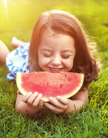 Closeup portrait of smiling child holding watermelon slice in the gardenの写真素材