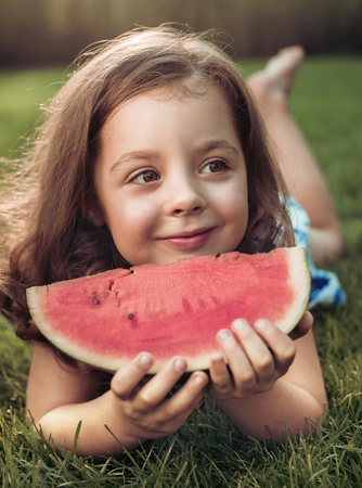 Closeup portrait of smiling child holding watermelon slice in the gardenの写真素材