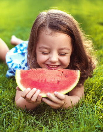 Closeup portrait of smiling child holding watermelon slice in the gardenの写真素材