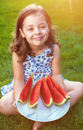 Portrait of smiling, cute girl holding watermelon slices in the gardenの写真素材