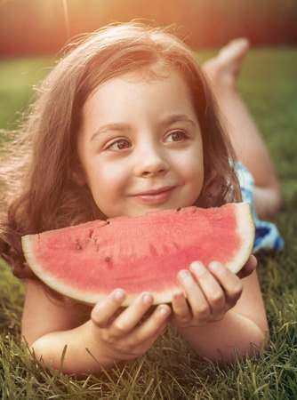 Closeup portrait of smiling child holding watermelon slice in the gardenの写真素材
