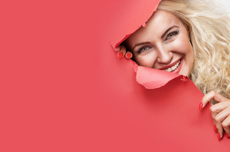Pretty blond woman looking from behind of a red paperの写真素材