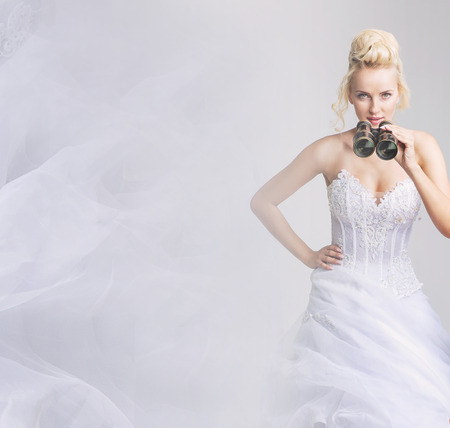 Cheerful, blond bride looking through the binocularsの写真素材
