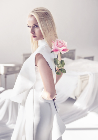 Elegant, young blond lady holding a beautiful pink roseの写真素材