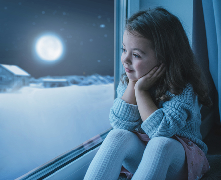 Cute, little girl looking at the moon the winter skyの写真素材