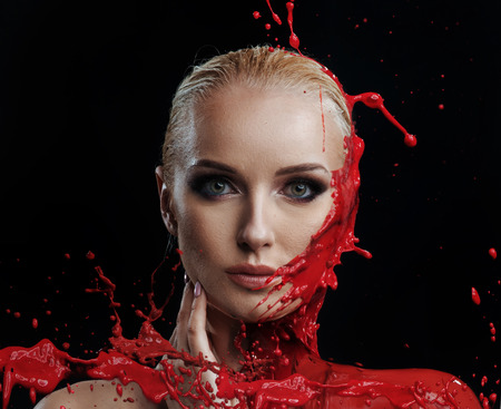Red paint splashing against a woman's young faceの写真素材